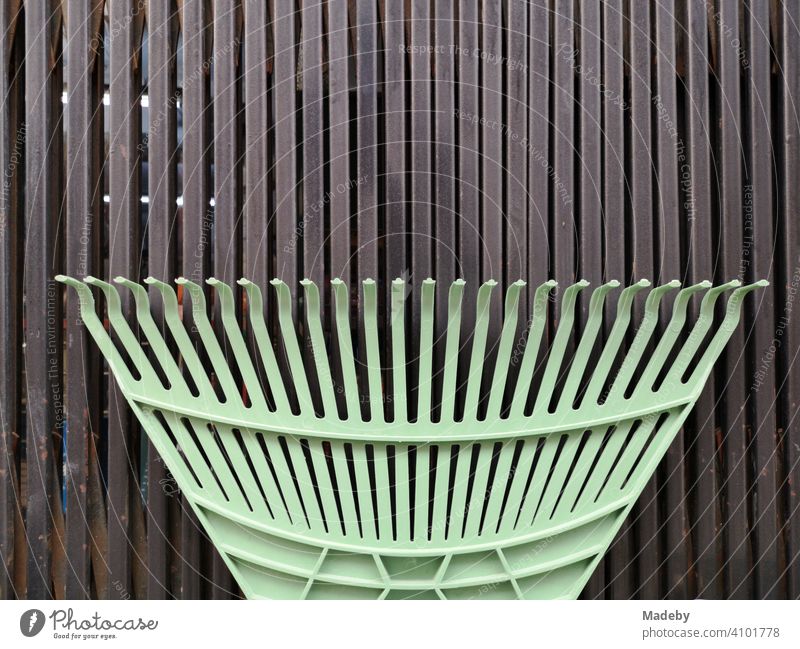 Green rake made of plastic for the garden in front of brown panel made of wood in the old town of Alacati near Cesme at the Mediterranean Sea in the province of Izmir in Turkey