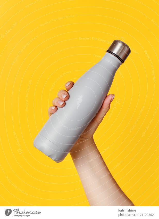 Hand with grey reusable insulated bottle on yellow background hand mockup ecologic water steel thermo aluminum blank close up concept copy space negative space