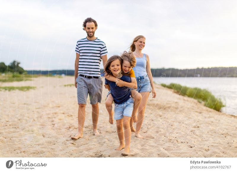 Young family having fun outdoors at the beach sea lake holidays vacation nature summer parents son boy kids children together togetherness love people happy