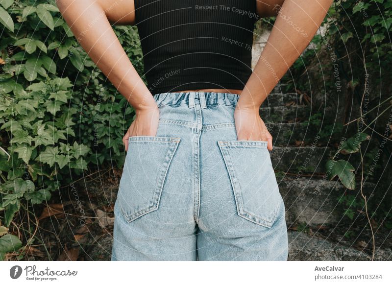 Back part of a woman wearing mom jeans surrounded by plants and modern style stylish waist people boyfriend denim garment high white young brother canvas