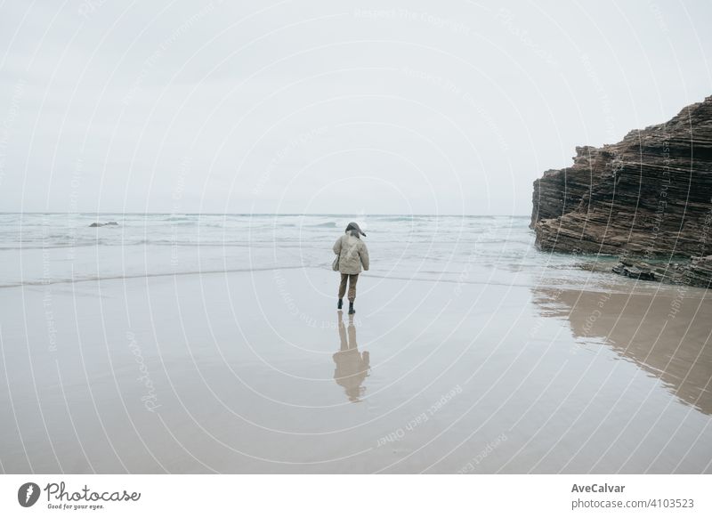 A young woman walking by the shore of the beach during a cloudy day, with copy space and liberty concept person female ocean loneliness senior solitude lonely
