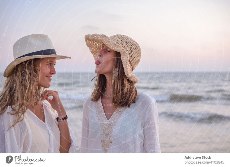 Smiling girlfriends in summer clothes barefoot in water on beach women sea traveling seaside charming vacation hat curly holiday together freedom journey