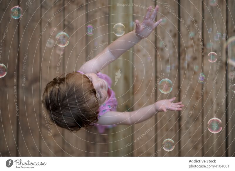 Joyful girl playing with colorful bubbles in wooden ground soap childhood joyful fun adorable cheerful park playful enjoyment action wet little motion
