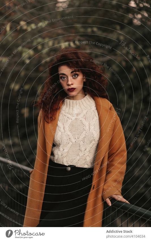 Pensive curly haired woman wearing casual standing in park pensive sensual young dark hair overcoat jumper railing knitted female thoughtful thinking trendy