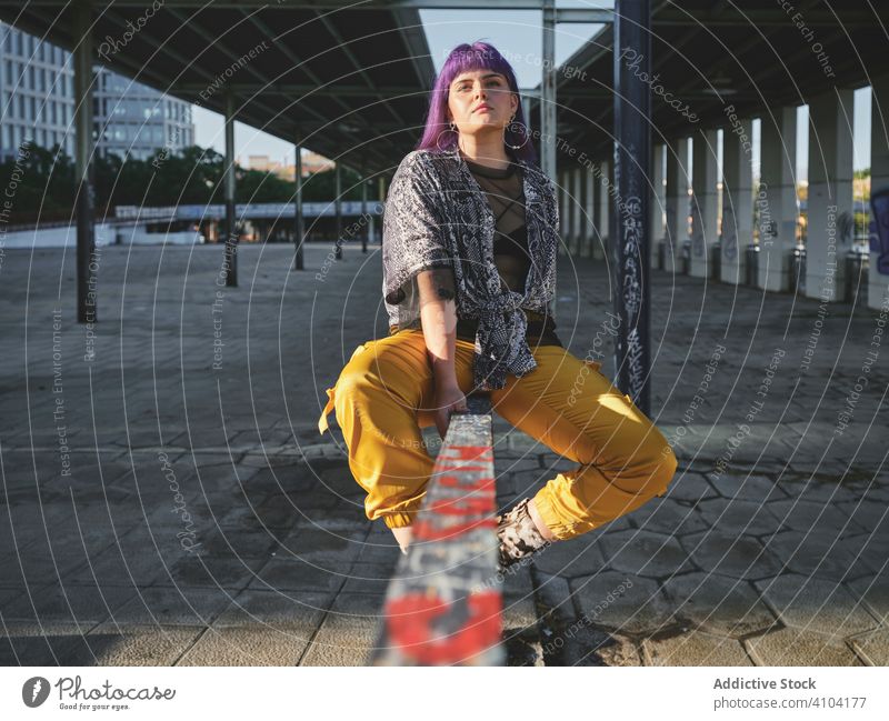 Woman with purple hair in yellow pants sitting on metal fence woman stylish hairstyle shiny wall fashion young urban model street human female outfit hipster