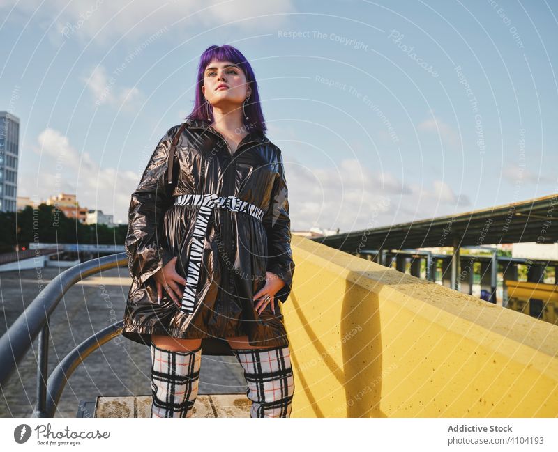 Woman with purple hair near metal construction woman stylish urban hairstyle jacket shiny fence yellow wall fashion young model street human female outfit