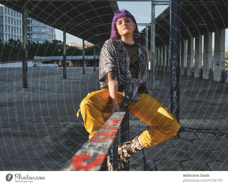 Woman with purple hair in yellow pants sitting on metal fence woman stylish hairstyle shiny wall fashion young urban model street human female outfit hipster