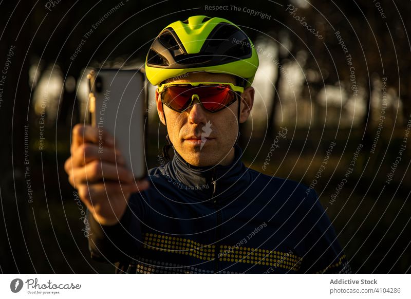 Man cycling in a park using mobile phone freedom helmet ride bicycle bike cyclist exercise fitness man person sport adventure healthy lifestyle nature road