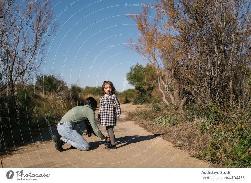 Mother tying shoelaces for child on path in countryside mother girl kid help daughter together weekend childhood day serious adorable lovely bonding calm