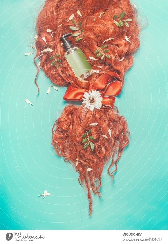 Red ginger hair tied in a ponytail with ribbon, green leaves, flowers  and cosmetic product bottle : shampoo, hair conditioner and care  on turquoise blue background. Beauty and hair styling concept