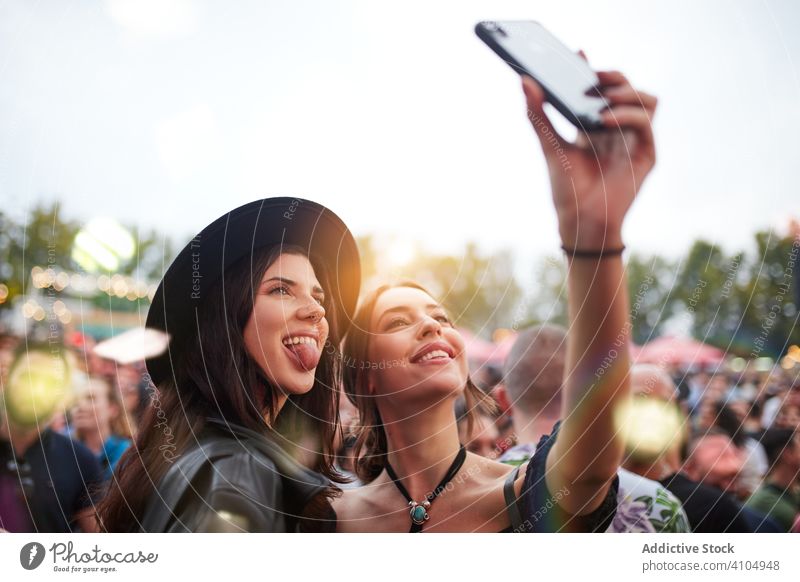 Joyful women taking selfies on smartphone fooling around and sticking out tongues in sunny day friend festival celebration friendship communication together