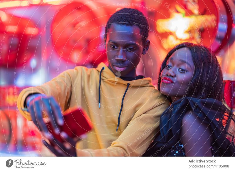 Black couple taking selfie on fairground smile smartphone ethnic night colorful illumination entertainment man woman fun boyfriend girlfriend black funfair