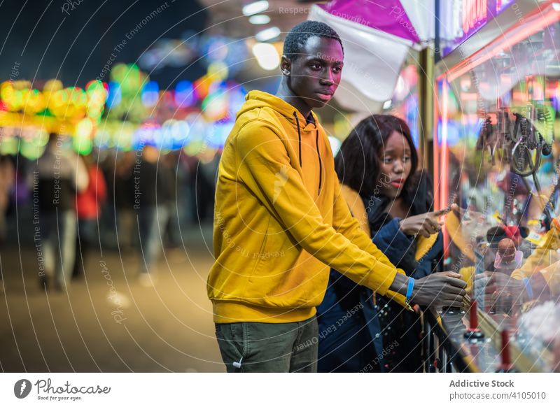 Black man playing claw crane for girlfriend couple funfair arcade together date evening catch toy watch woman entertainment game smile cheerful happy focused