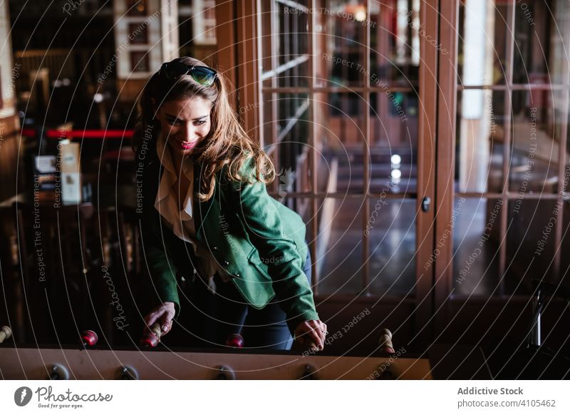 Satisfied trendy lady enjoying play table football playing woman game stylish cafe smiling laughing outfit fashionable young casual standing female clothes