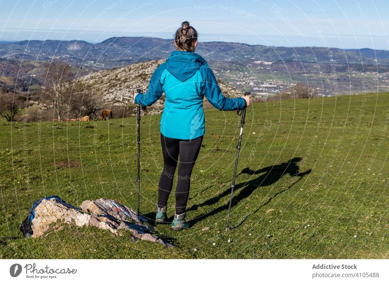 Anonymous female tourist with trekking poles on meadow hike mountain using hill rock green sunlight hiking woman activewear trip nature summer travel activity
