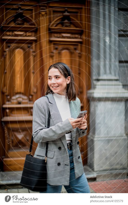 Positive female in casual wear with smartphone on city street woman using standing walking browsing surfing mobile smile laugh enjoy connection outfit device