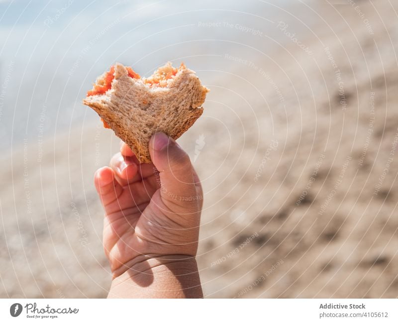 Little child holding bread on beach girl eat summer sunny daytime cloudy sky kid hood apparel garment pastry piece fresh bite food lifestyle rest relax coast