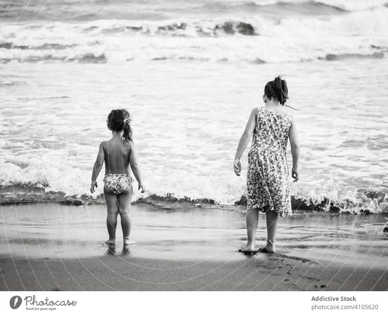 Anonymous sisters near waving sea beach wave water sand wet family together summer sibling girl kid child nature lifestyle rest relax coast shore ocean little