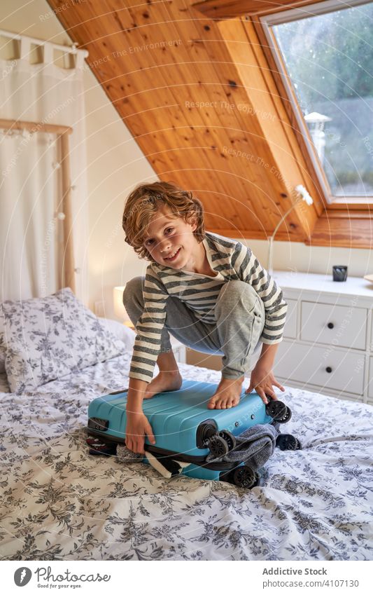 Boy sitting on top of luggage on bed boy pack suitcase bedroom cozy home kid child holiday trip vacation travel clothing clothes apparel garment preparation