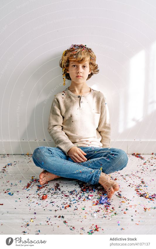 Child in casual wear playing with confetti at home boy child male teen colorful sitting floor modern crossed legs childhood lifestyle celebrate holiday festive