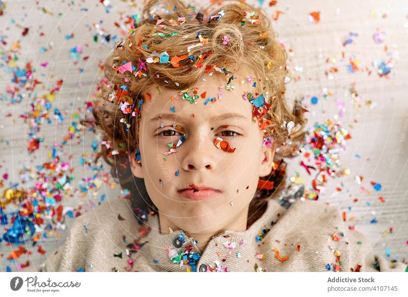 Beautiful boy with face covered in confetti home emotionless fun colorful lying preteen floor modern childhood lifestyle celebrate holiday festive event