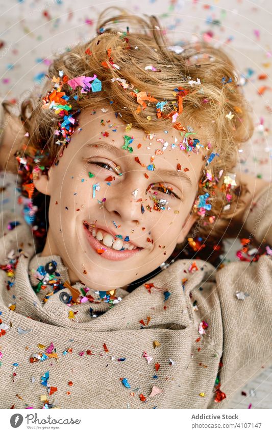 Beautiful boy with face covered in confetti home emotionless fun colorful lying preteen floor modern childhood lifestyle celebrate holiday festive event