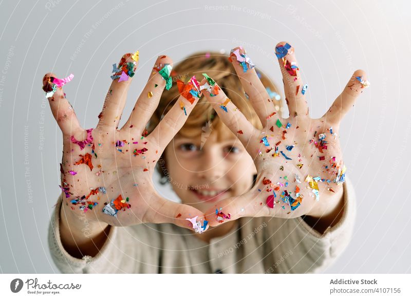 Content boy showing hands in confetti palm child fun enjoy laugh smile colorful teen demonstrate celebrate holiday festive event generation kid junior blond
