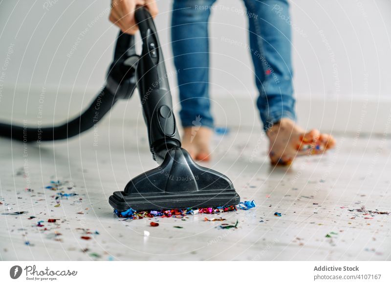 Unrecognizable guy vacuuming floor with confetti after party clean mess home barefoot leg jeans remove apartment housekeeping domestic equipment colorful modern