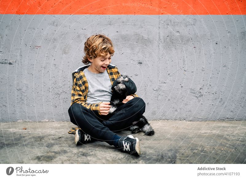 Boy with puppy sitting next to concrete wall child dog boy street building affection care little breed canine purebred animal cuddle domestic friendly kid pet