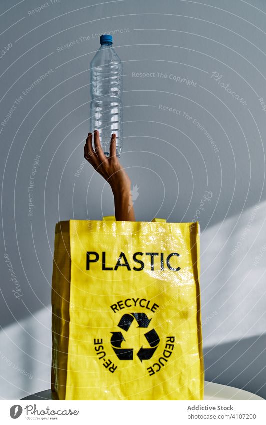 Anonymous person holding plastic bottle in studio stick out bag hand water empty recycle trash garbage environment polluted waste problem rubbish ecology