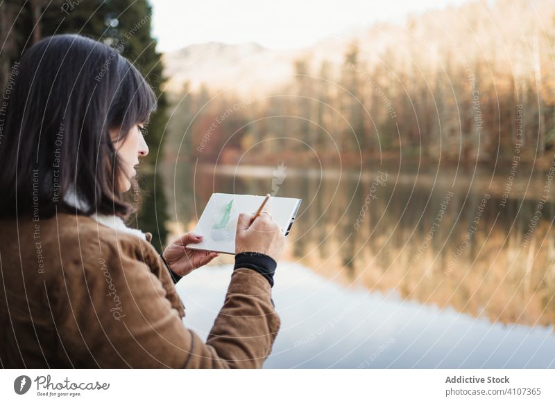 Woman standing at lakeside and drawing in notebook woman forest landscape tranquil nature autumn picture painter scenic female young artist water tree beauty