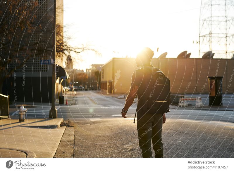 Anonymous man walking on the street during sunset city casual young enjoy outfit backpack contemporary stylish lifestyle modern ethnic hispanic latino downtown