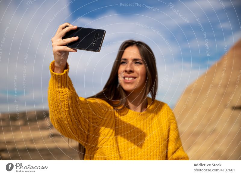 Pleased woman taking selfie on smartphone with big rock during vacation shooting using mobile phone cliff mountain stone blue sky nature smile enjoy travel