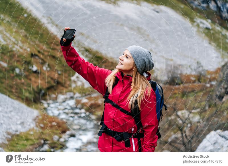 Woman with backpack taking selfie on smartphone on background of mountains woman tourist using travel nature device gadget dry peak photographing trekking