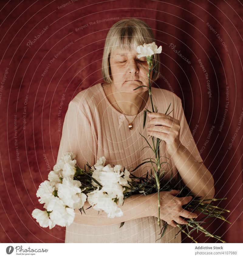 Pensive elderly woman with flowers at home old carnation bouquet floral natural gift fresh female spring celebrate fragrant event holiday festive peaceful