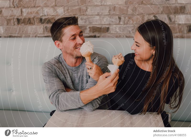 Happy couple eating ice cream cones while having date in cafe flirt dessert love joy feed cheerful smile relationship care relax pleasure together treat calorie