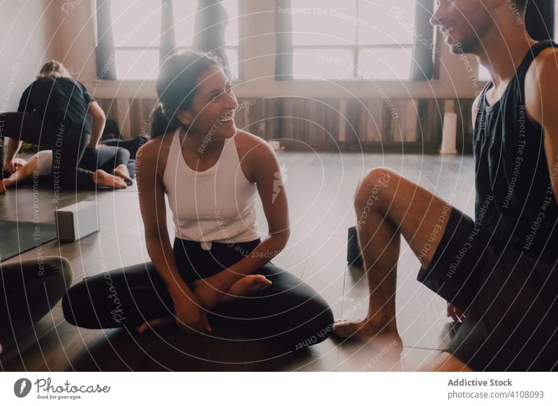 Group of multiracial athletes talking to each other while relaxing together after practicing yoga in light modern workout room friend lotus pose rest
