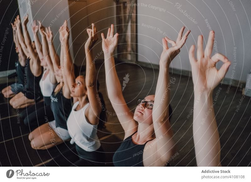 Group of calm focused athletes practicing yoga together performing hero pose in contemporary gym meditate virasana stretch gyan mudra exercise training