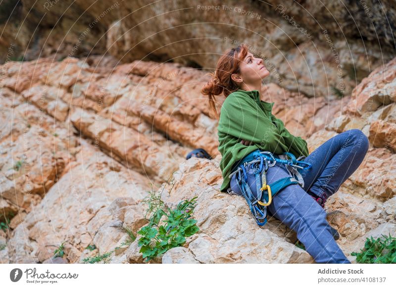 Focused young female alpinist resting on cliff in summer woman climber break stone extreme challenge equipment rock adventure contemplate casual hobby sport