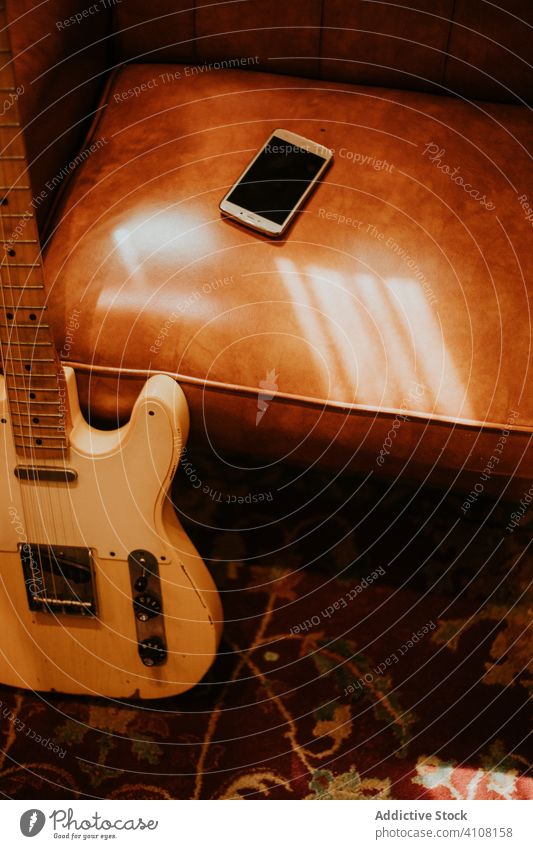 Guitar leaning on sofa with smartphone in room guitar using old instrument music sound gadget entertain melody acoustic rock classic empty screen home detail