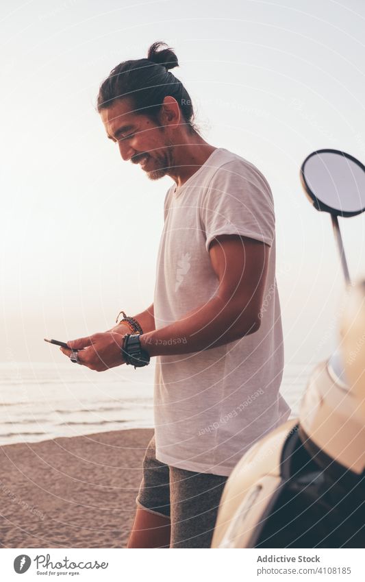 Happy active man using phone at seaside happy cheerful bike sporty smartphone male casual ocean beach ethnic guy adult motorbike message reading browsing
