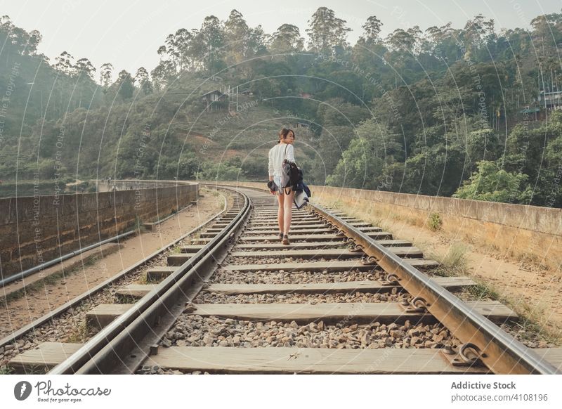 Anonymous female tourist walking on lonely railway against exotic forest woman empty green bridge plant tourism travel nature lifestyle countryside railroad