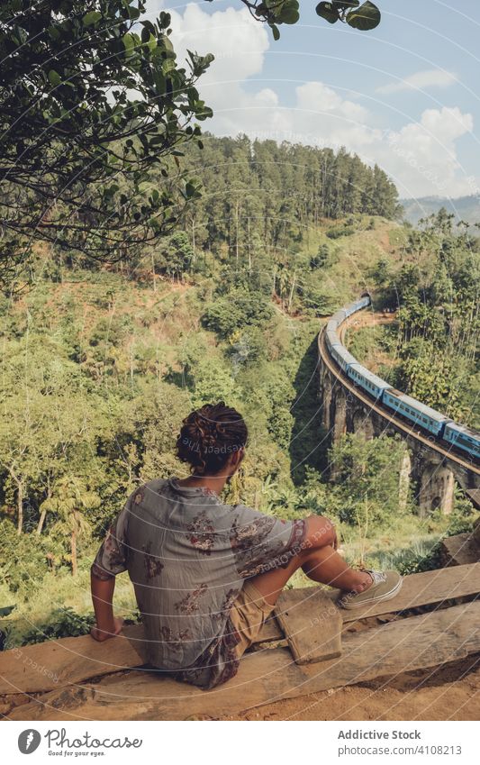 Anonymous man on vacation enjoying view from peak of hill viewpoint tourism bridge landscape tropical travel train railroad trip green tree plant nature journey