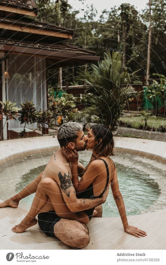 Couple on vacation kissing on poolside couple resort sensual hotel tropical honeymoon nature hug embrace male female together swimsuit relationship exotic