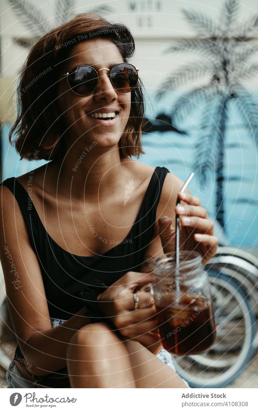 Joyful female traveler in sunglasses drinking cocktail woman resort tropical summer lounge cheerful exotic tourism relax smile rest laugh enjoy beverage