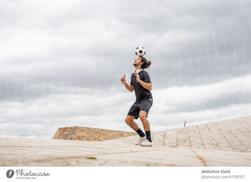 Man training with soccer ball against cloudy sky man football kick city urban street sport sportsman game activity player athlete motion sportswear guy summer