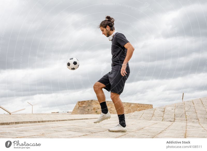 Man training with soccer ball against cloudy sky man football kick city urban street sport male sportsman game activity player athlete motion sportswear guy
