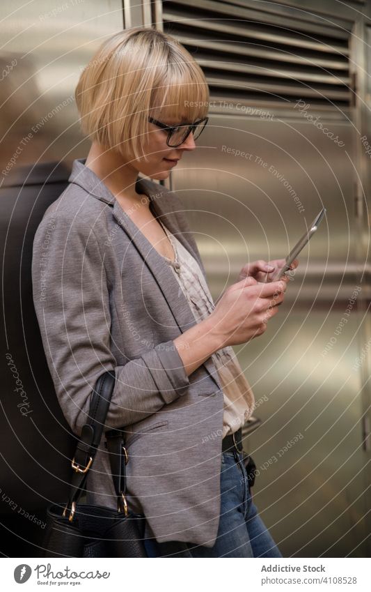 Woman leaning on wall and using tablet businesswoman stylish young female professional person beautiful attractive entrepreneur elegant browsing texting surfing