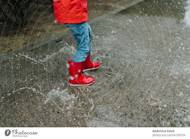Active kid jumping in puddle in park alley child messy season funny water wet dirt childhood weather mud autumn game active rubber boots raincoat botanical
