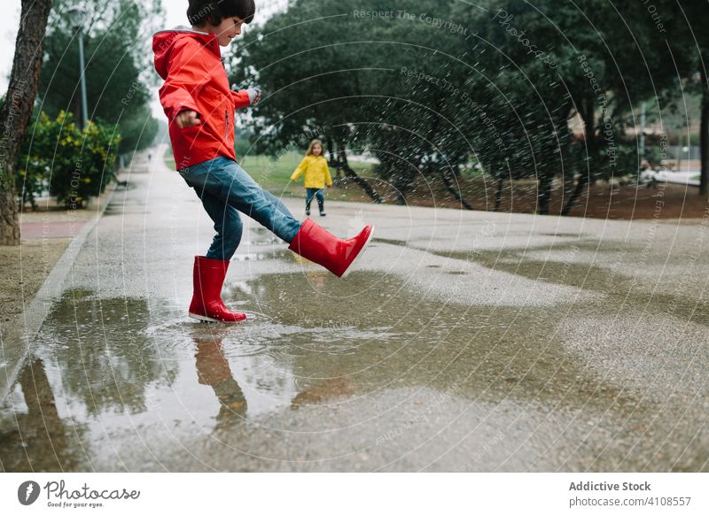 Funny kids playing in puddle in park alley children messy weather together siblings season funny water wet dirt childhood mud autumn game active rubber boots